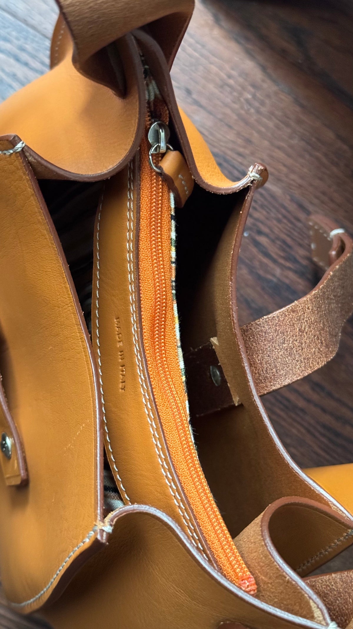 Close-up of tobacco Eugenia leather hobo bag showing its closed zip, metal slider, leather pull, contrast stitching, and Made in Italy stamp.
