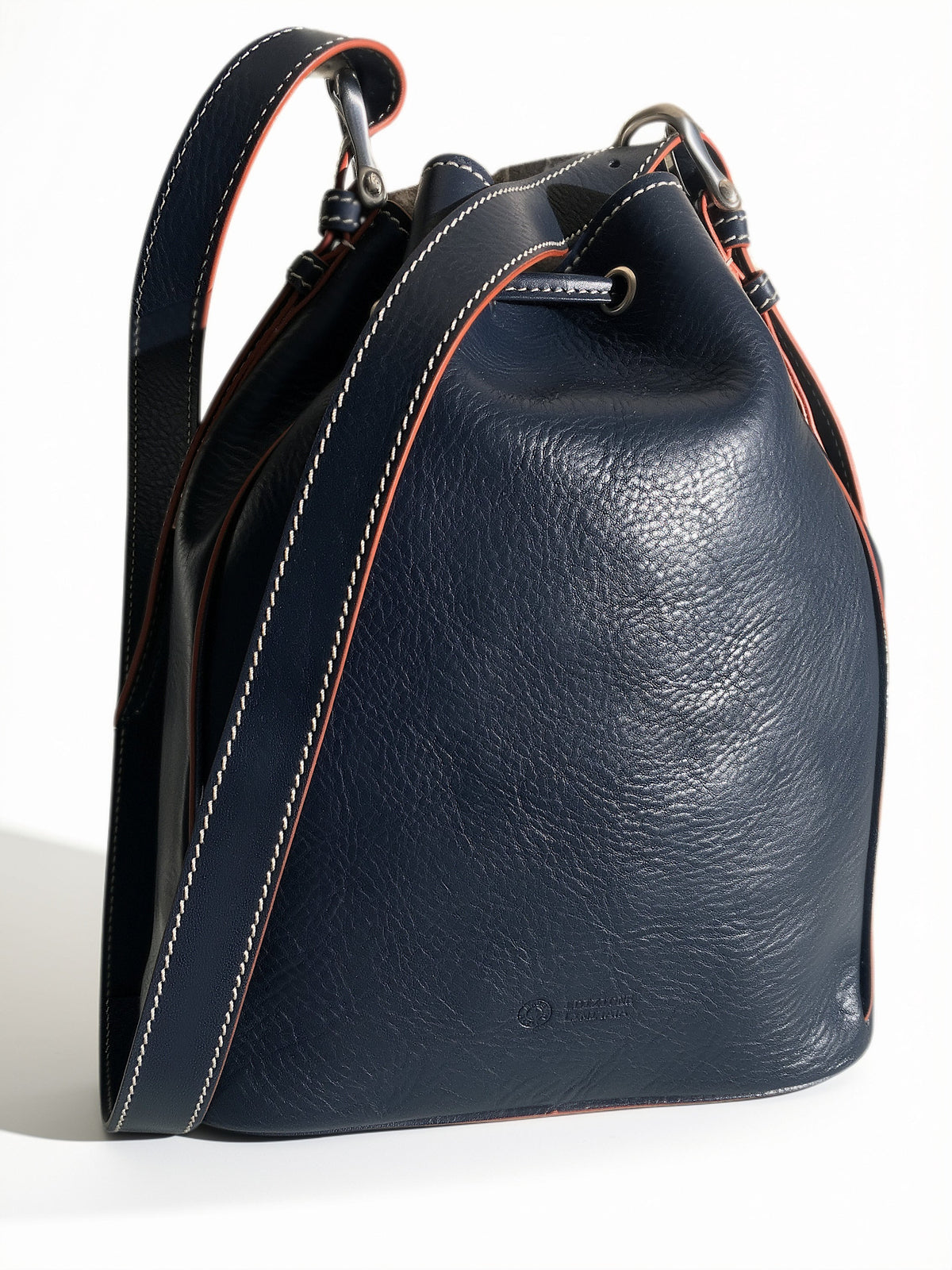 Rear view of blue Febe leather bucket bag showing leather grain, embossed logo, contrasting trim, and shoulder strap.
