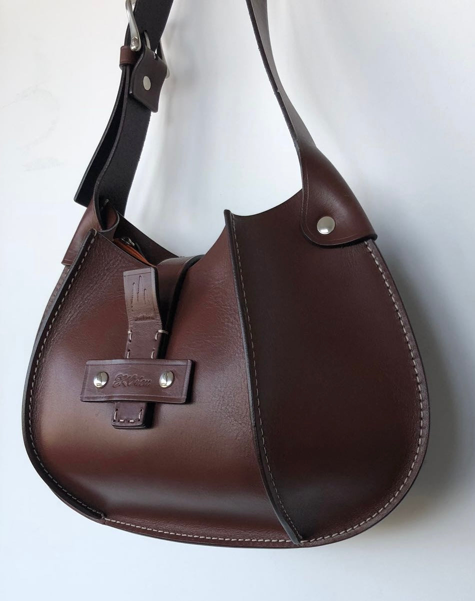 Dark brown Eugenia leather hobo bag viewed at an angle, showing curved side panels, contrast stitching, a central leather fastening, and riveted strap attachments.