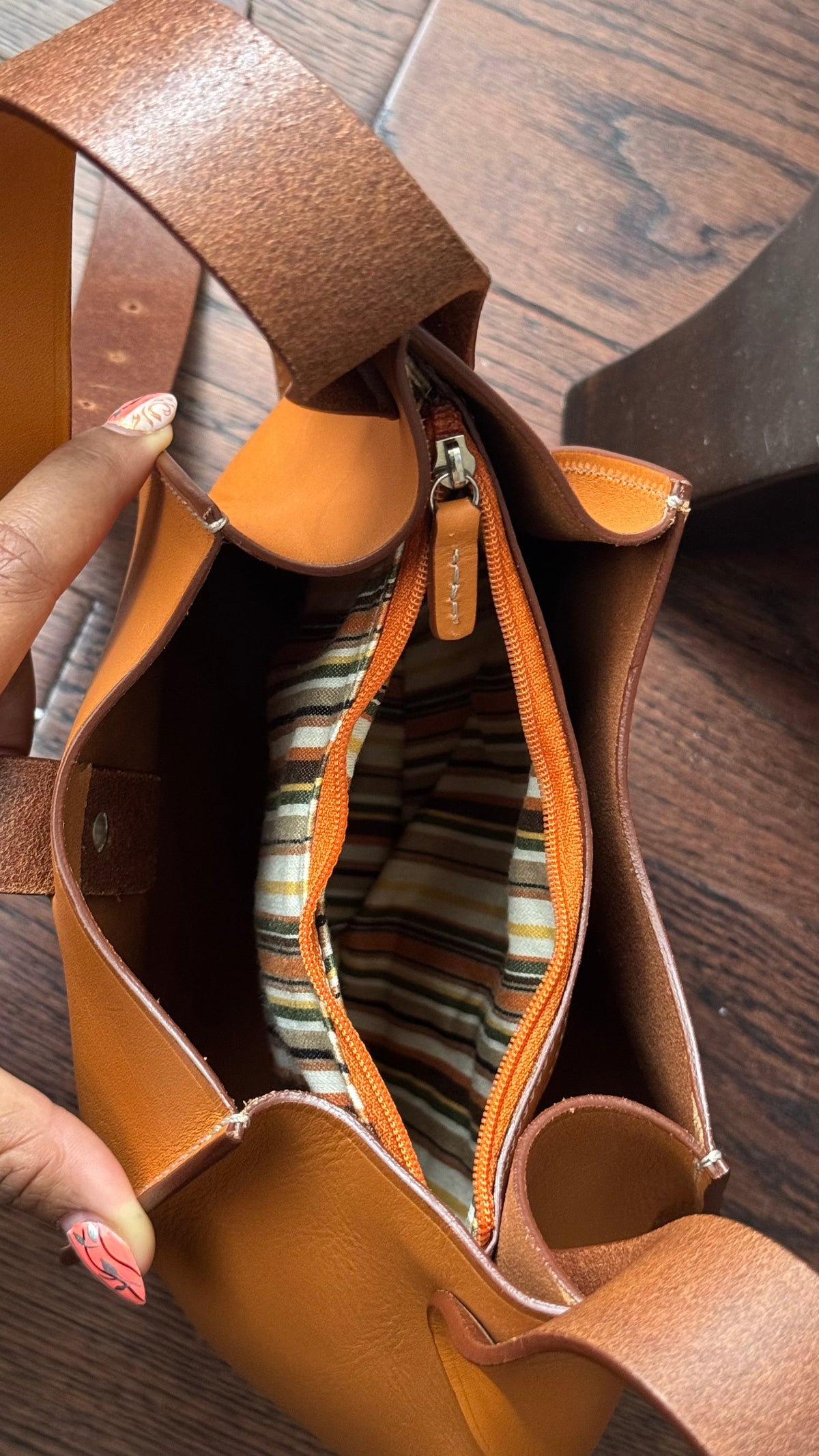 Open tobacco Eugenia leather hobo bag held apart to show its empty striped lining and zippered opening.