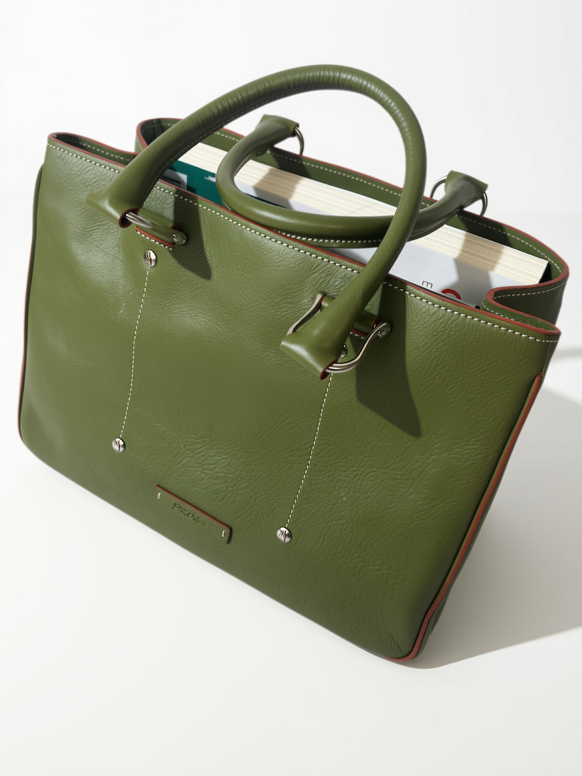 Green Allegra leather tote bag viewed at an angle, showing rolled handles, metal attachments, stitched detailing, and books inside.