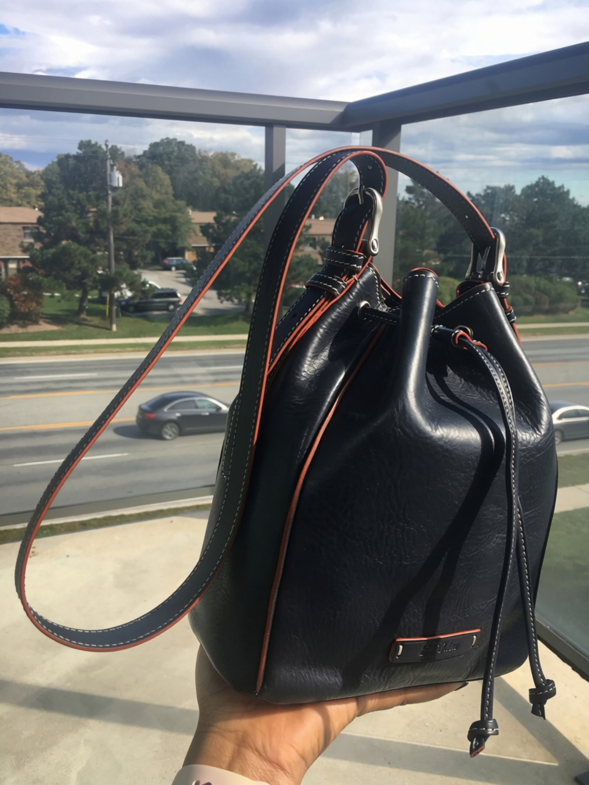Blue Febe leather bucket bag held in one hand outdoors, showing its size, drawstring closure, and shoulder strap.